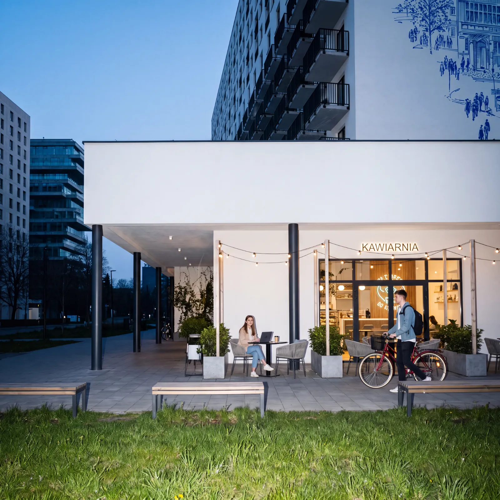 The ground floor of a residential development with a café at dusk